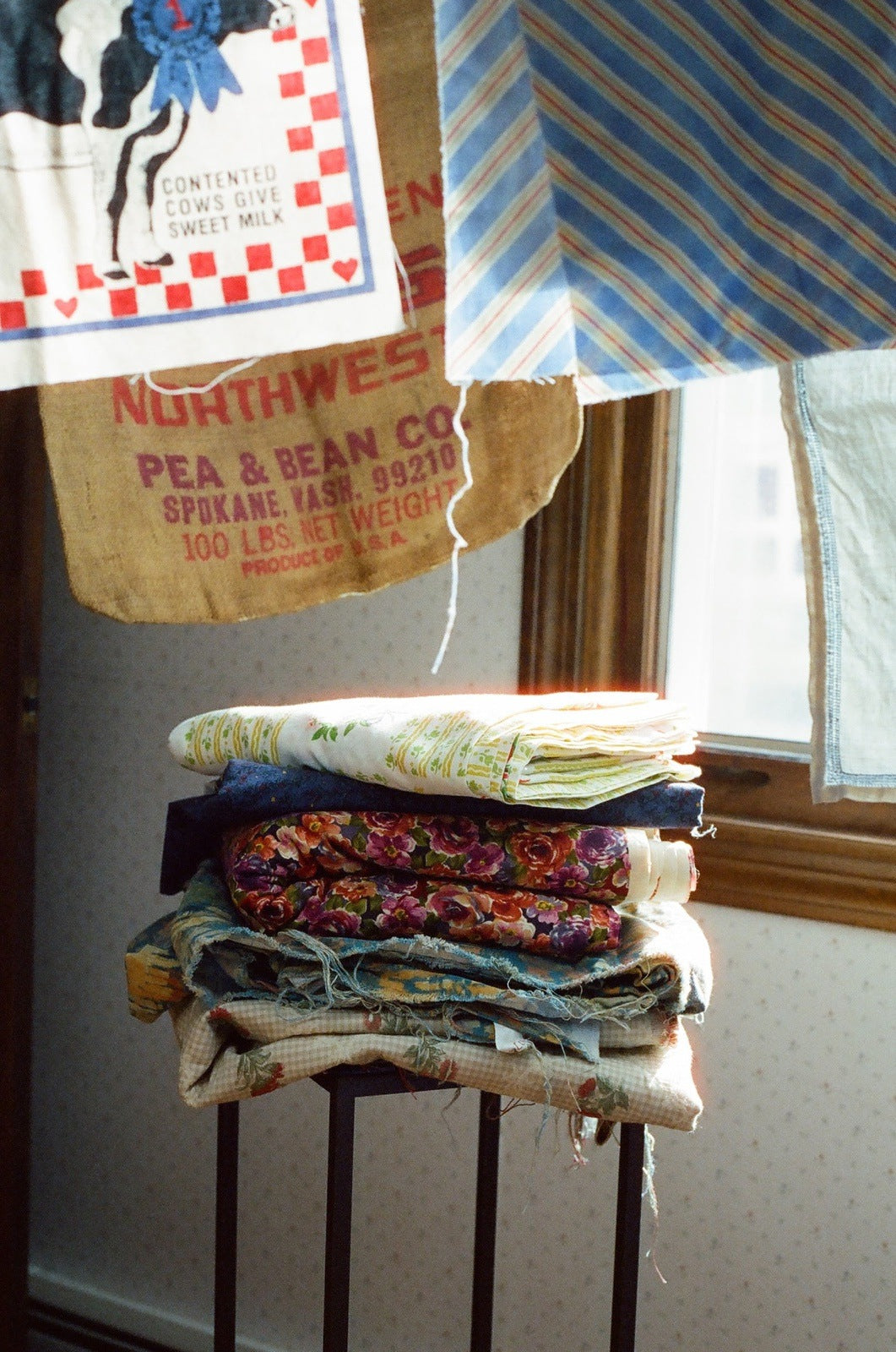 a pile of folded up fabric on a small end table with fabric hung from a clothes line above